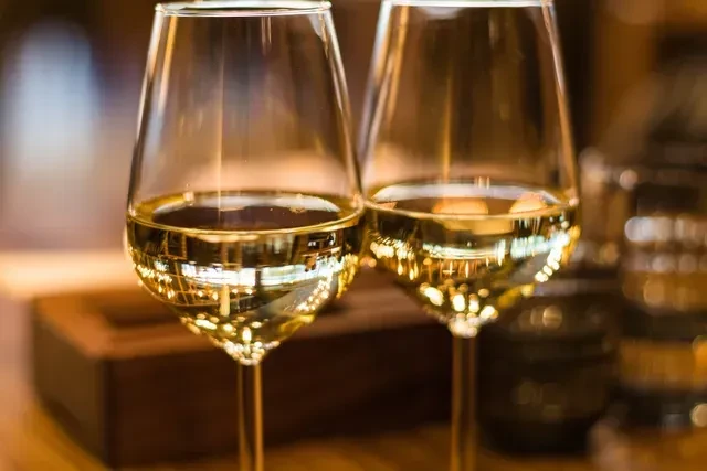 Two clear wine glasses with pale yellow wine, warm bokeh background.