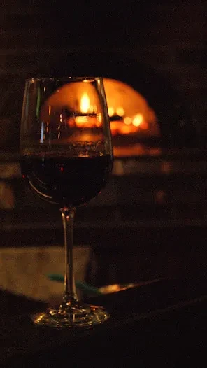 Red wine glass in foreground, blurred glowing oven in background.