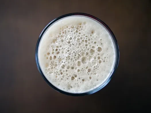 Overhead shot of a glass beverage topped with thick, bubbly off-white foam.