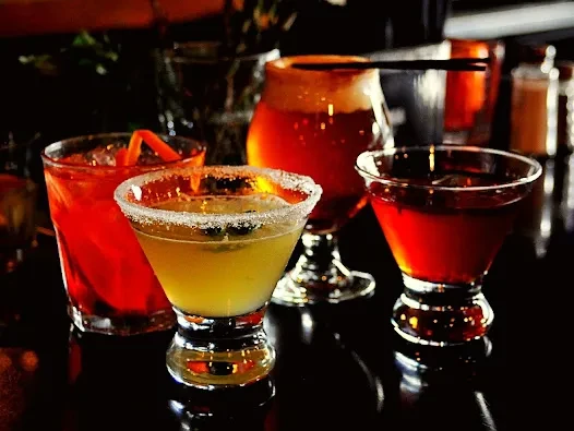Four distinct alcoholic beverages on a dark, reflective bar top.