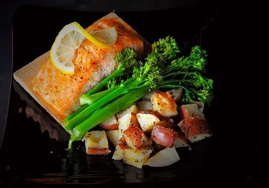 Plated salmon, broccolini, roasted potatoes, and toast on dark plate.