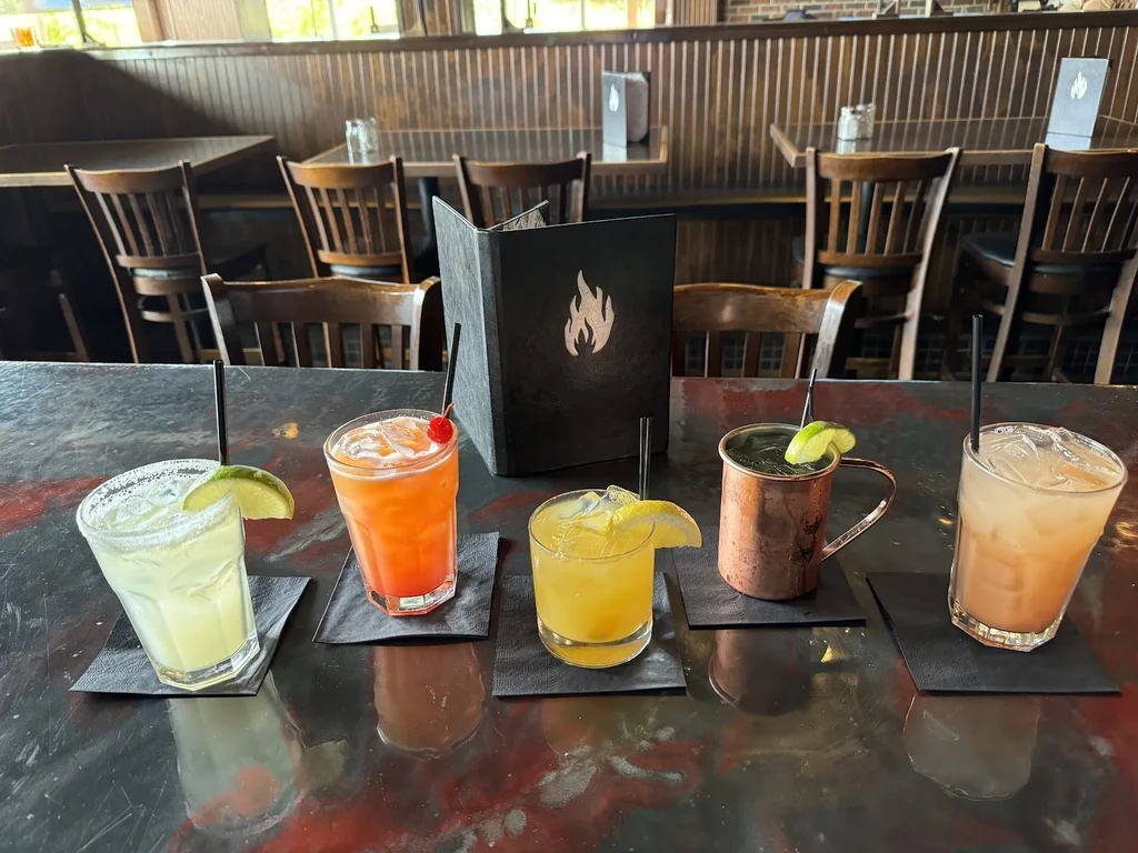 Five varied drinks on a dark bar in a restaurant.
