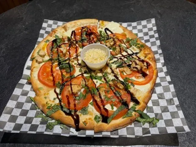 Pizza with chicken, tomatoes, melted cheese, basil, balsamic, and Parmesan cup.