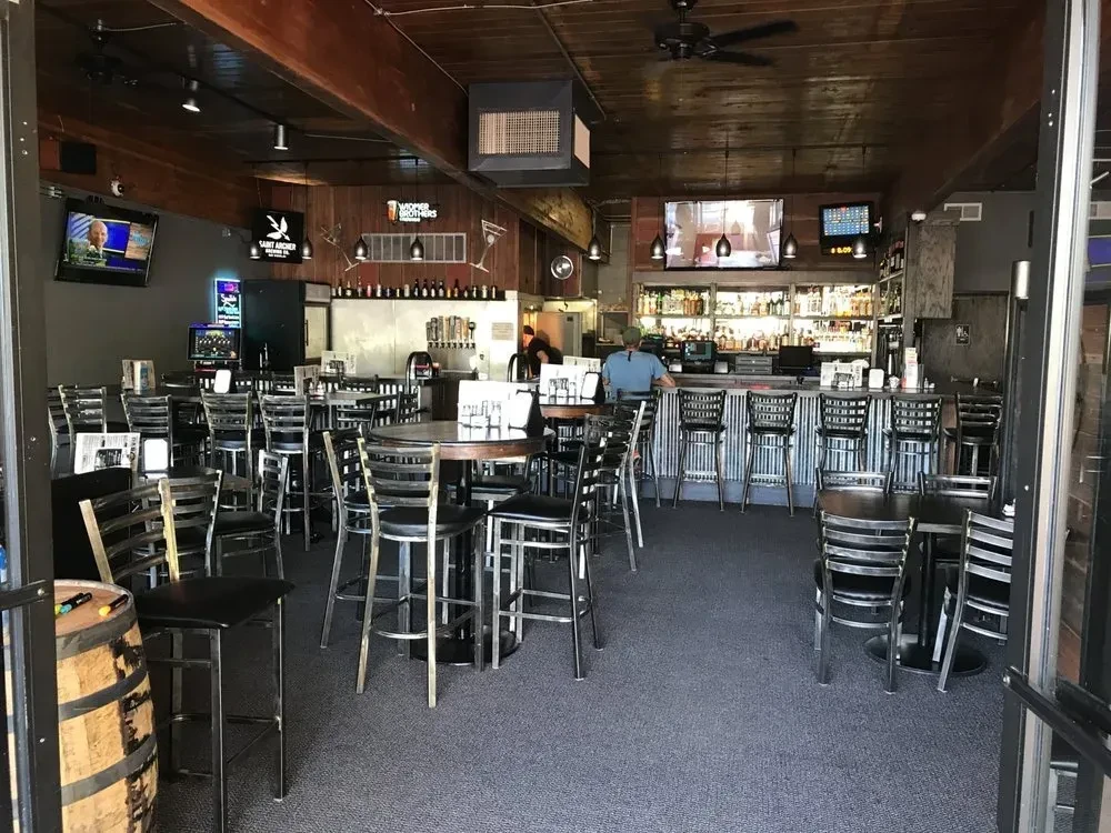 Rustic-industrial bar interior with high-top tables, TVs, and a prominent bar.