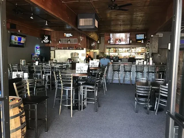 Casual bar interior with high-top tables, a stocked bar, and TVs.