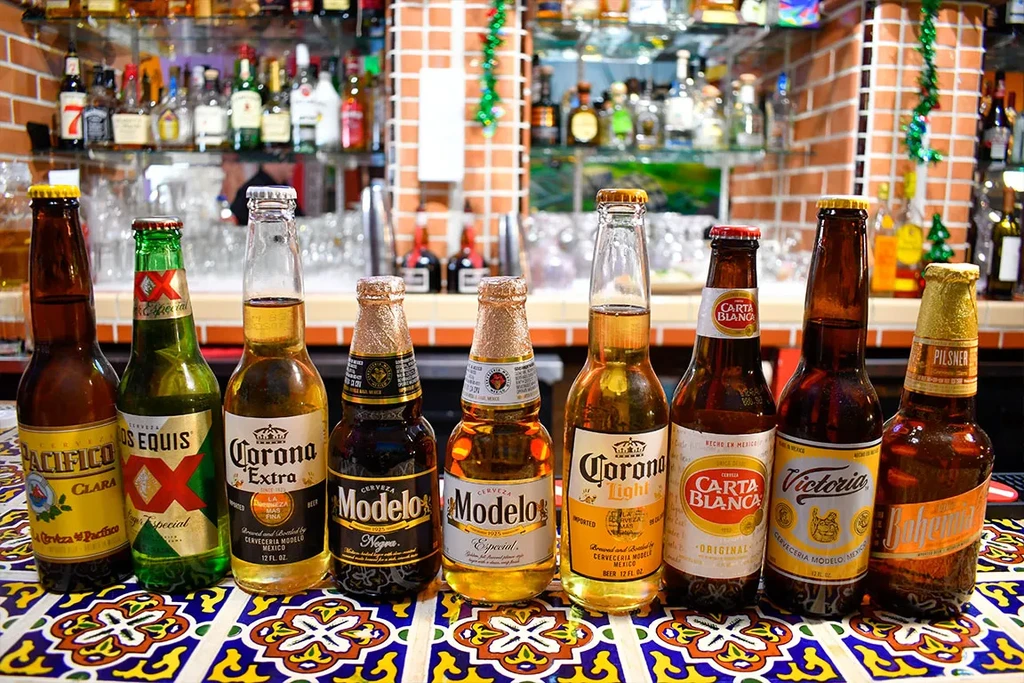 Nine bottled Mexican beers on a colorful tiled bar counter.