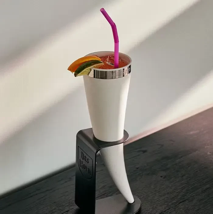 Pink drink in a white horn cup with citrus garnish.