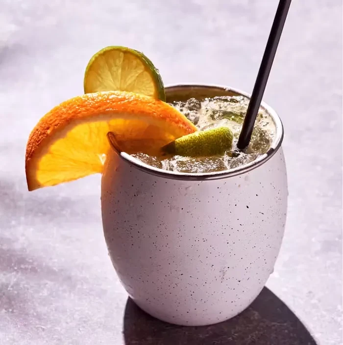 Chilled cocktail with citrus garnish in a speckled metal cup.