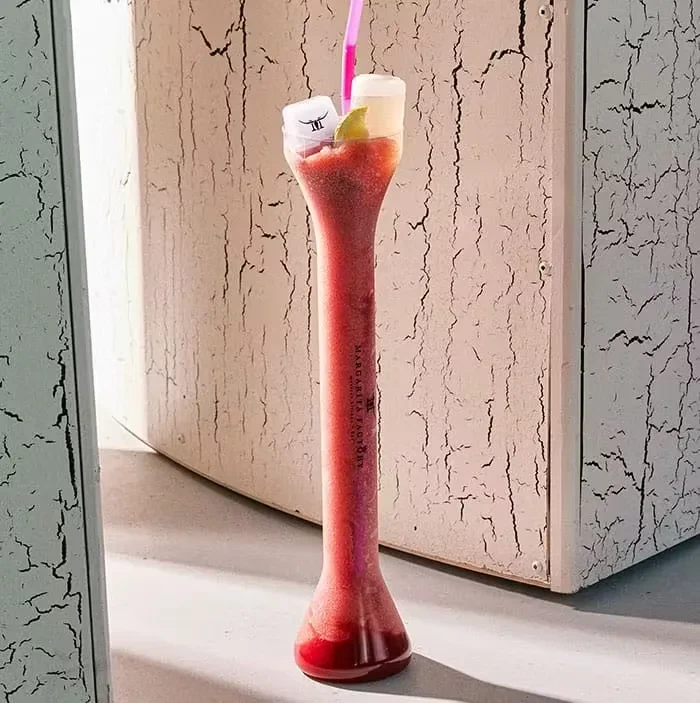 Tall, unique glass of frozen red-pink drink with lime and logo cubes.