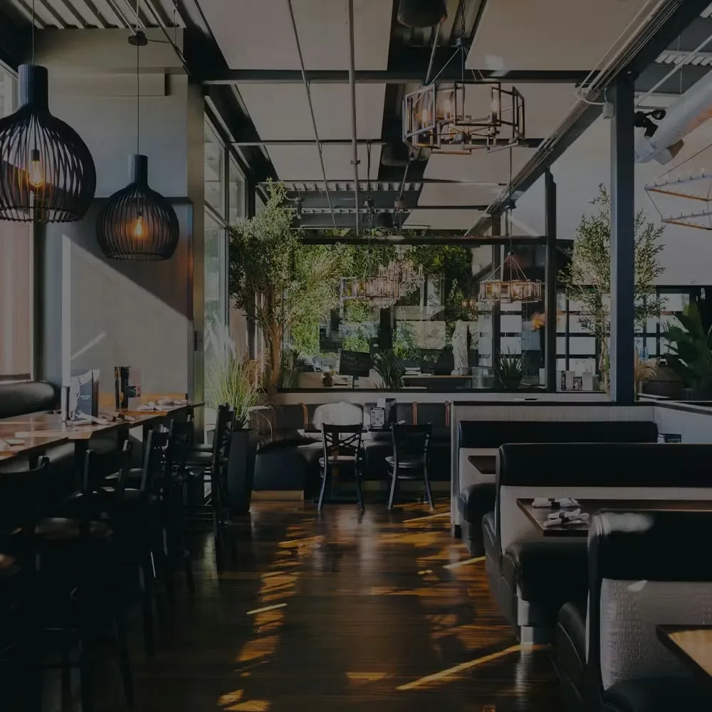 Empty modern restaurant with dark booths, industrial ceiling, and window view.