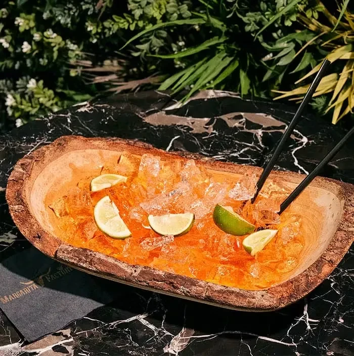 Rustic wooden trough with orange drink, ice, lime, straws, foliage.