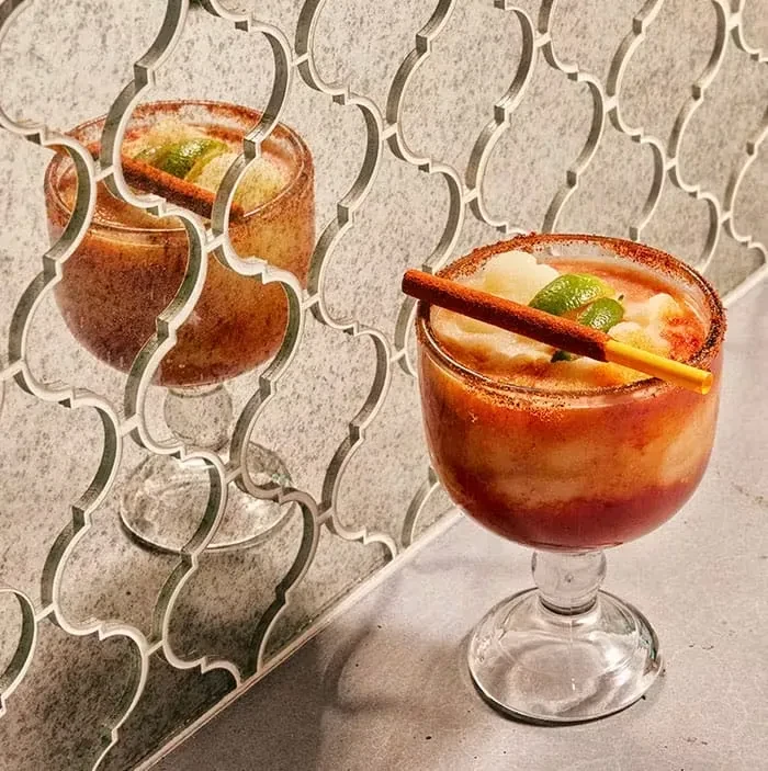 Vibrant layered frozen drink with spiced rim, lime, and sticks.