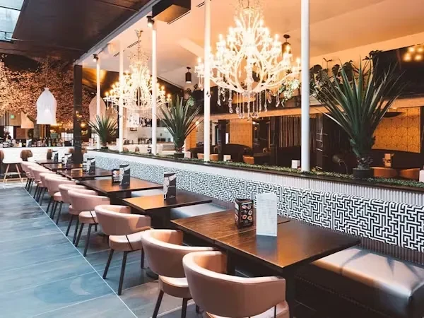 Modern restaurant dining area with geometric wall, chandeliers, and plants.