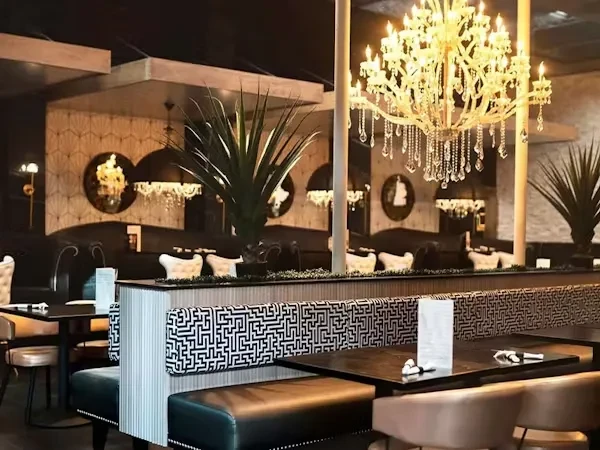 Upscale restaurant interior with dark leather booth, ornate chandelier, and plants.