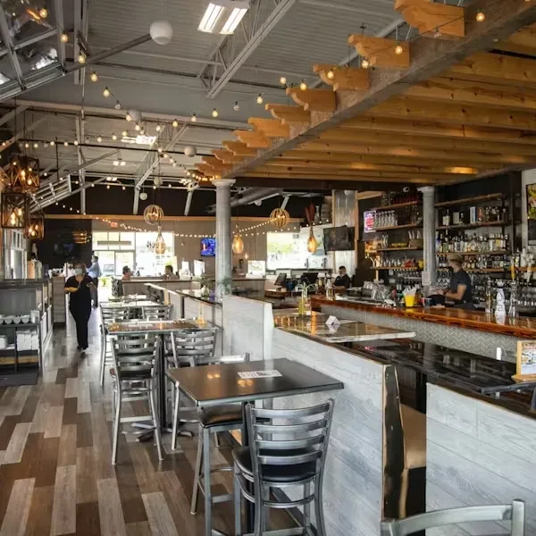 Modern industrial restaurant interior with high ceilings and a bustling bar.