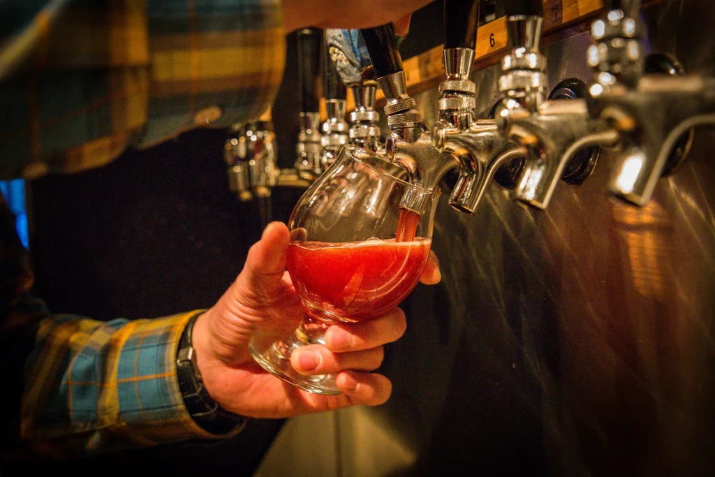 Hand fills stemmed glass with reddish beverage from a beer tap.