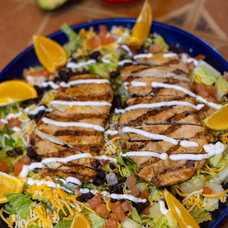 Large grilled chicken salad with creamy dressing, beans, and orange garnish.