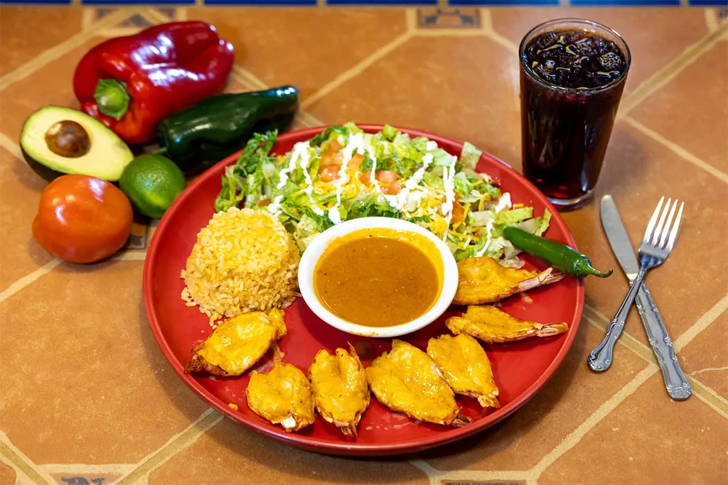 Mexican shrimp, rice, salad meal with fresh produce on tiled table.