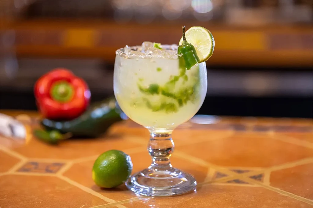 Muddled green cocktail with salted rim, lime, and chili garnish.