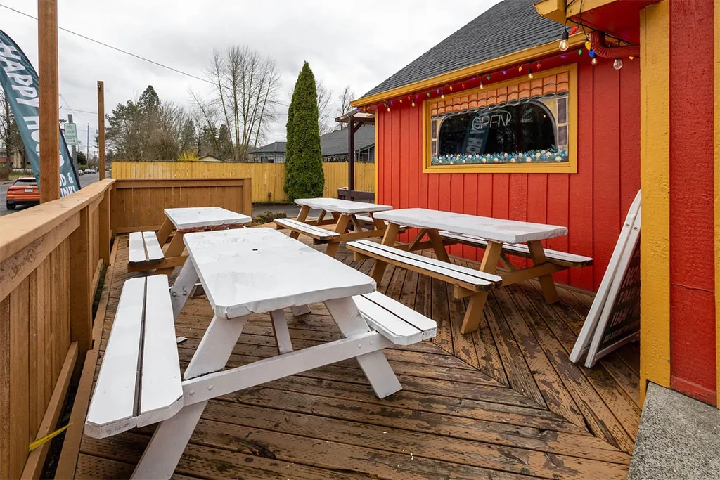 Outdoor restaurant with white picnic tables and red building, 'OPEN' sign.