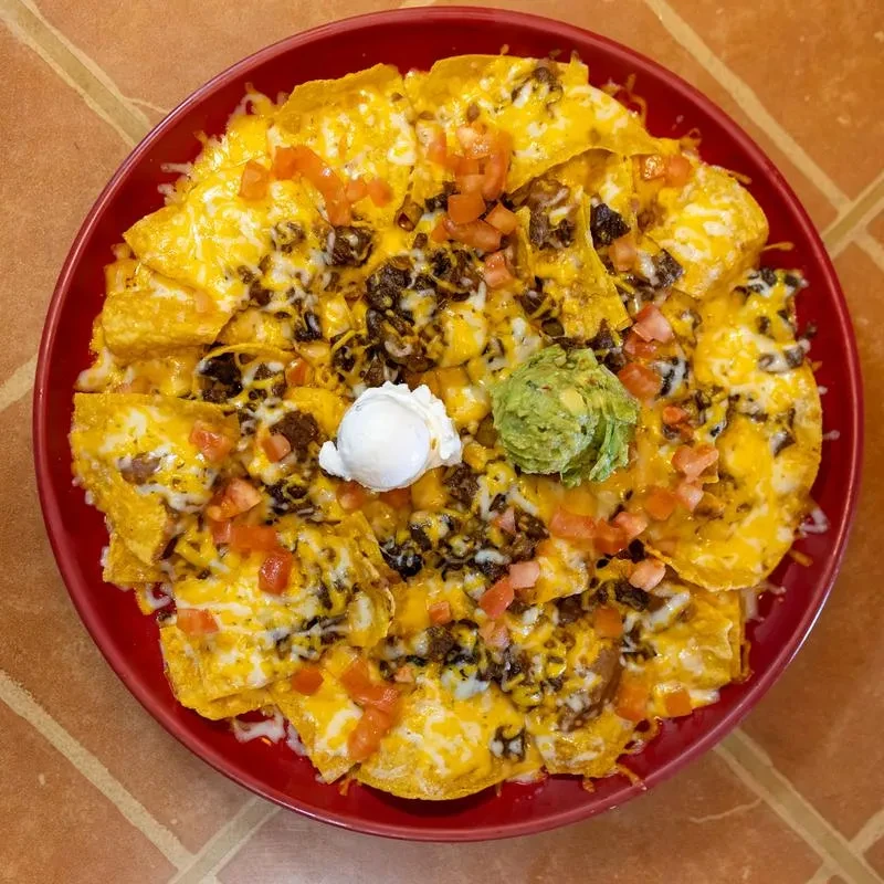 Loaded nachos with cheese, ground beef, tomatoes, guacamole, and sour cream.