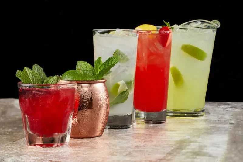 Still life of five colorful, garnished, icy drinks on stone.