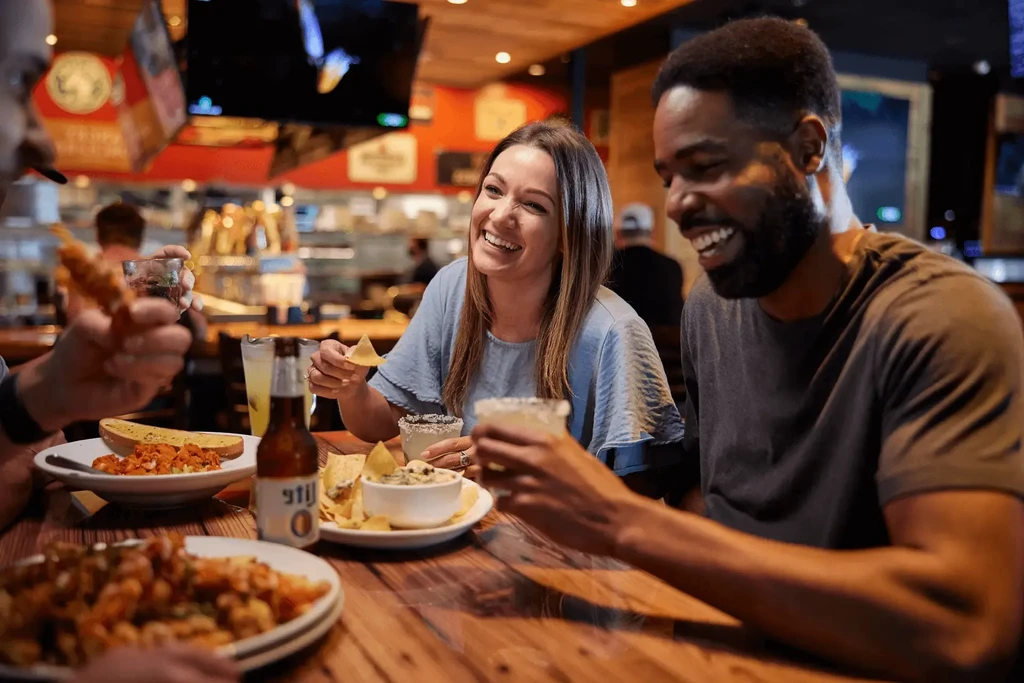 Smiling man and woman enjoying food and drinks at a restaurant table.