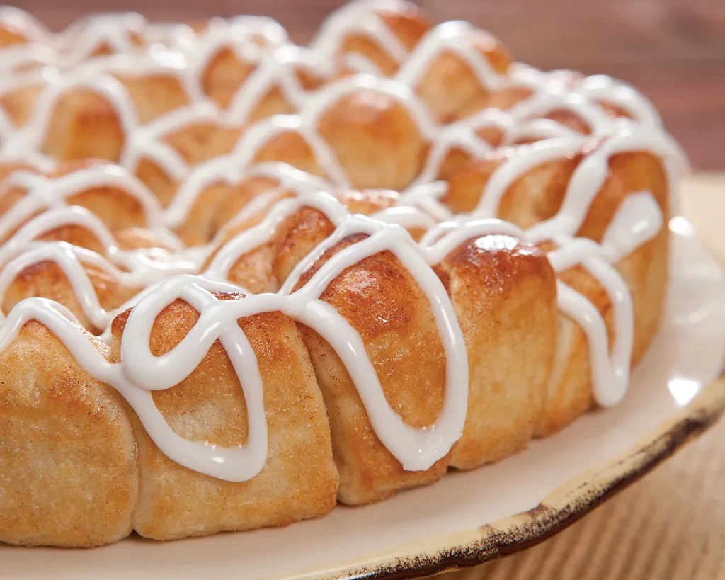 Golden-brown pull-apart bread with thick white icing on a ceramic plate.