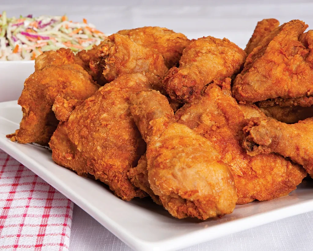 Large pile of crispy fried chicken on platter with coleslaw and checkered napkin.