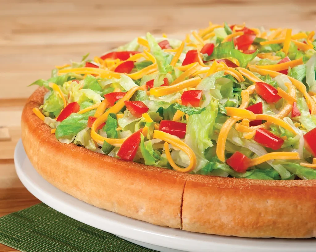 Deep-dish pizza crust topped with lettuce, peppers, and cheddar cheese.