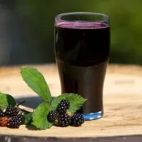 Tall glass of dark berry juice with blackberries on rustic wood.