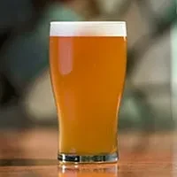 A pint glass of amber beer with white foam on a wooden surface.