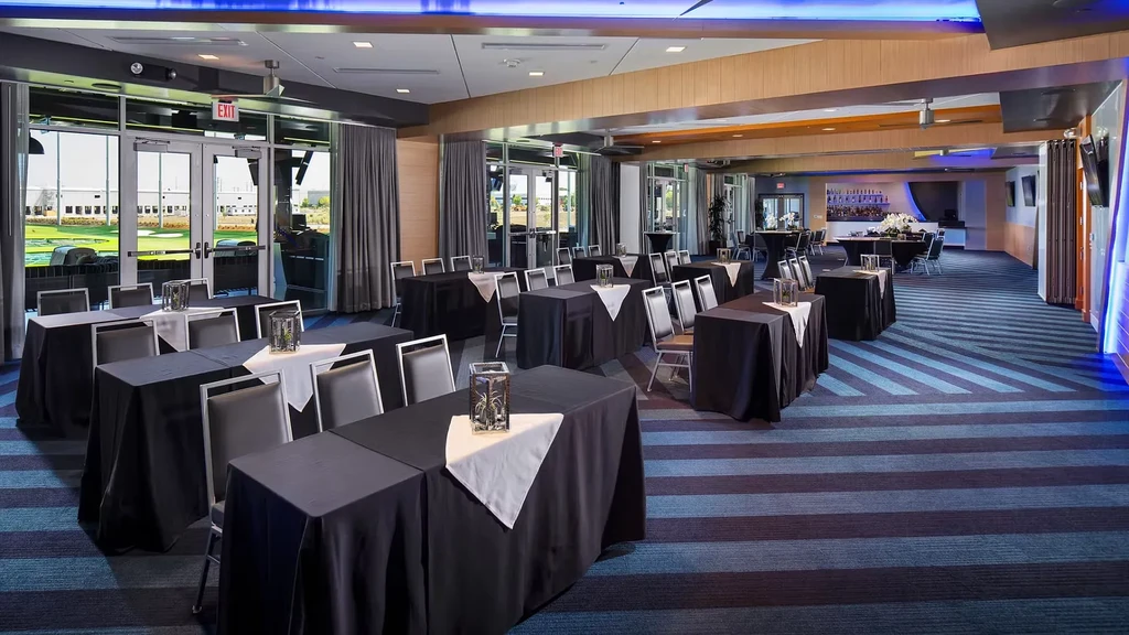 Modern event hall with tables, bar, overlooking a golf range.