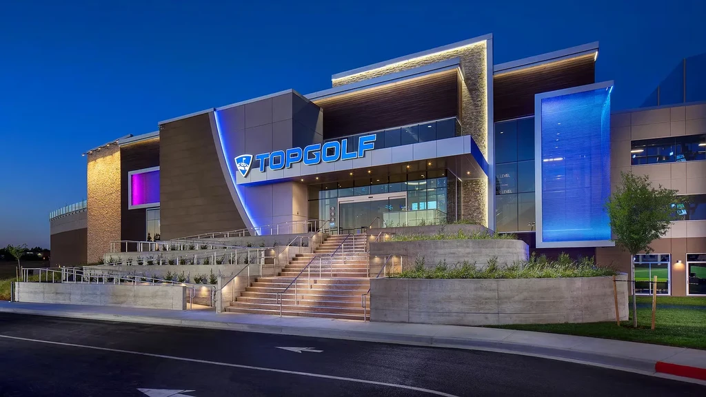 Topgolf facility exterior at twilight with blue and purple LED lighting.