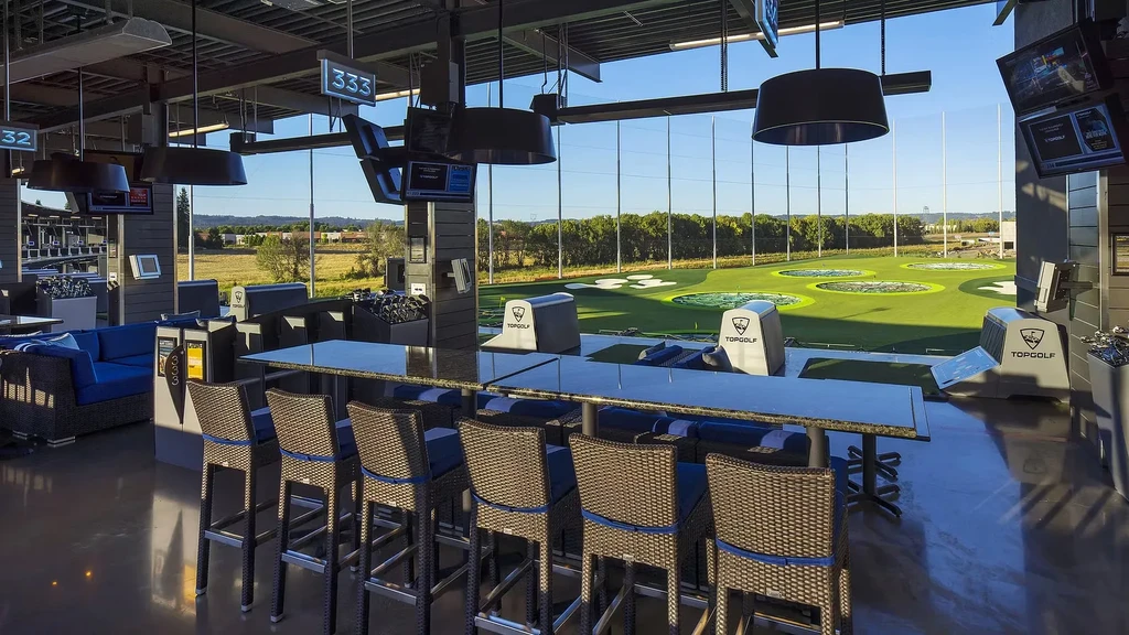 Empty Topgolf bay, indoor seating overlooks sunny outdoor golf range.