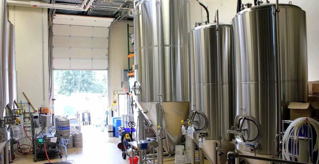 Interior of a brewery with large stainless steel tanks and stacked kegs.