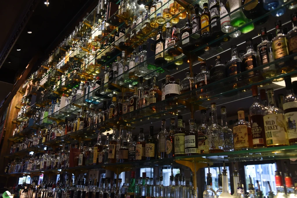 Extensive collection of liquor bottles brightly lit on multiple bar shelves.