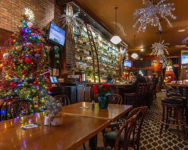 Festive bar with Christmas tree, liquor wall, ladder, tinsel, and patrons.