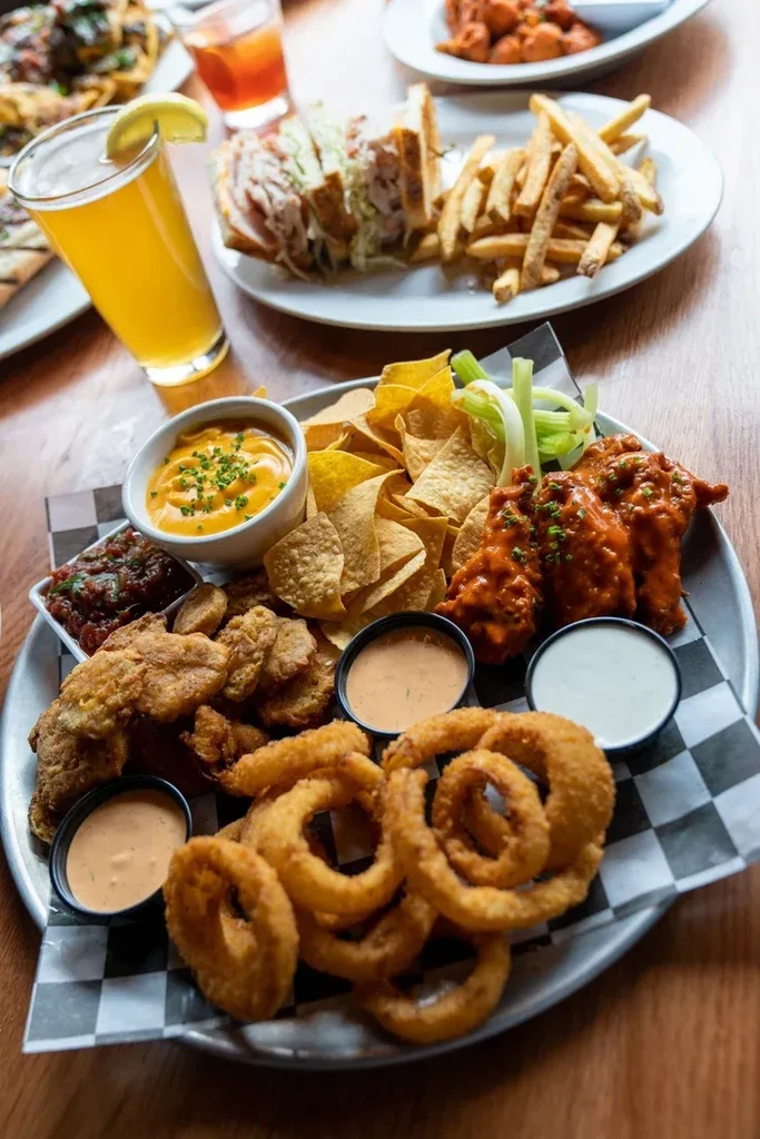 Platter of fried appetizers, sandwich, fries, and drinks on table.