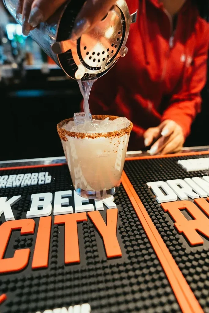 Bartender pours spiced-rim cocktail from shaker into glass with ice.