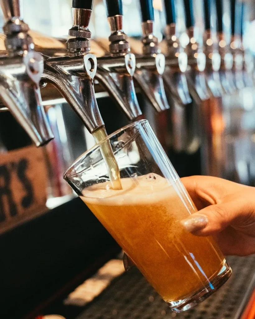 Hand holds glass as beer pours from tap, creating foam.
