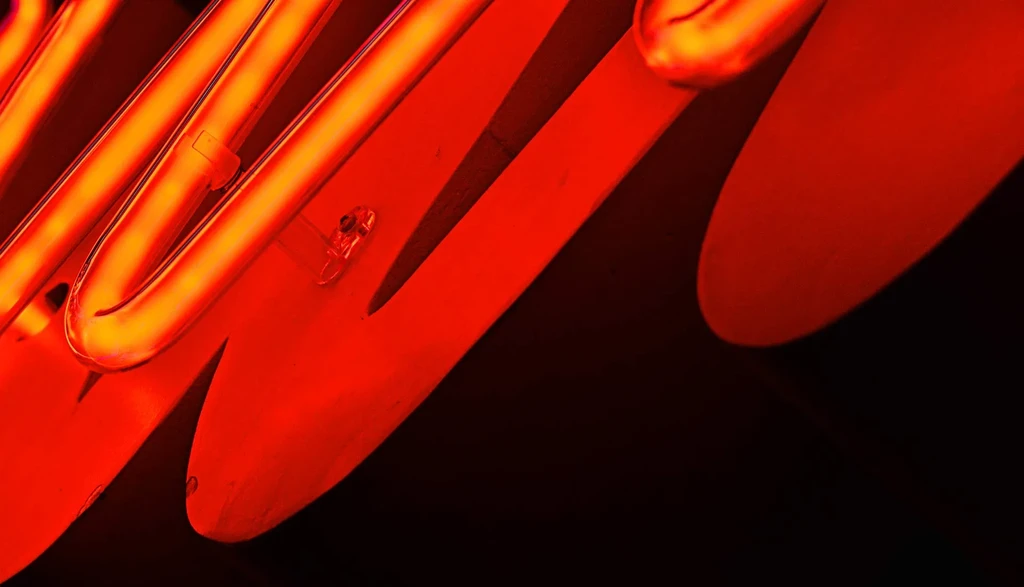 Vibrant orange-red neon sign with abstract curves on a dark background.