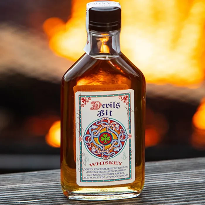 Devils Bit whiskey bottle with ornate Celtic label and fiery background.