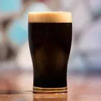Pint glass of dark stout beer with a creamy off-white head.