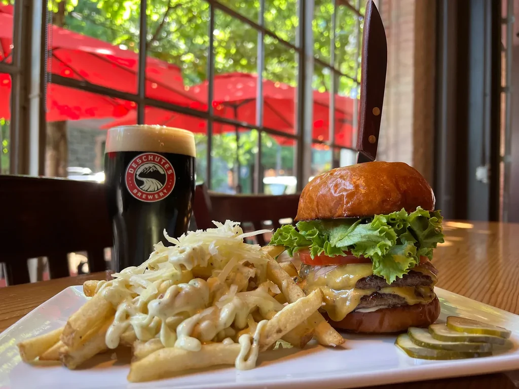 Cheeseburger, loaded fries, and Deschutes dark beer on a wooden table.