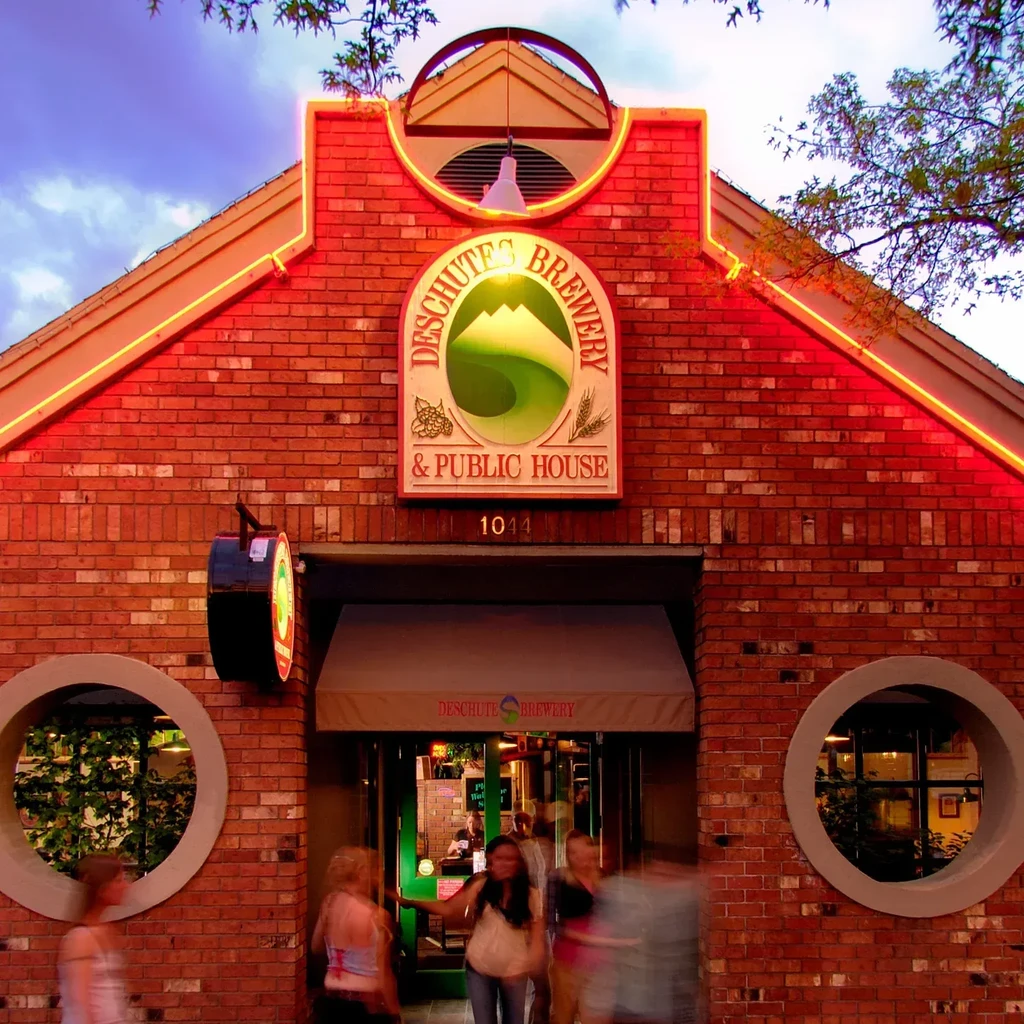 Illuminated Deschutes Brewery brick building with vibrant neon lights and blurred people.