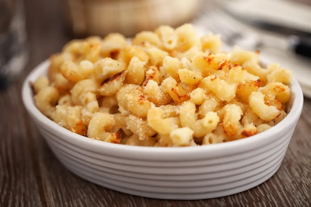 White bowl of golden-brown baked macaroni and cheese on a wooden table.