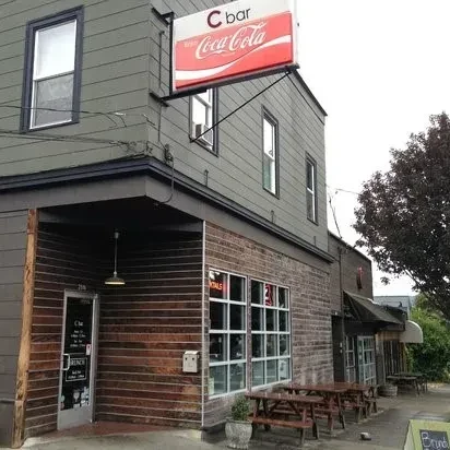 Dimly lit exterior of "C bar" with Coca-Cola sign and picnic tables.