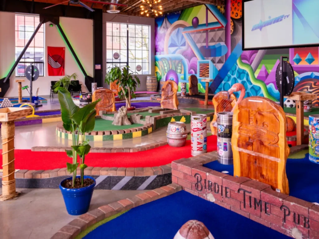 Vibrant indoor mini-golf course and pub with "BIRDIE TIME PUB" wall.