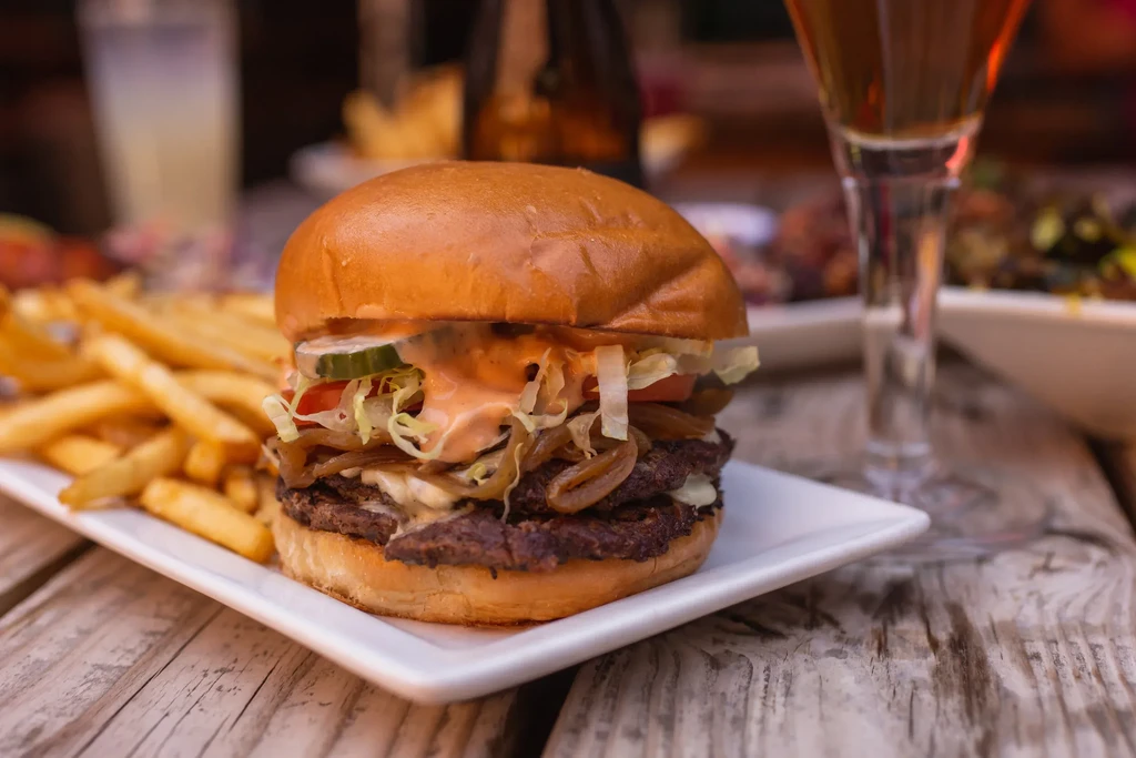 Double-patty burger, crispy fries, and beer on a wooden table.